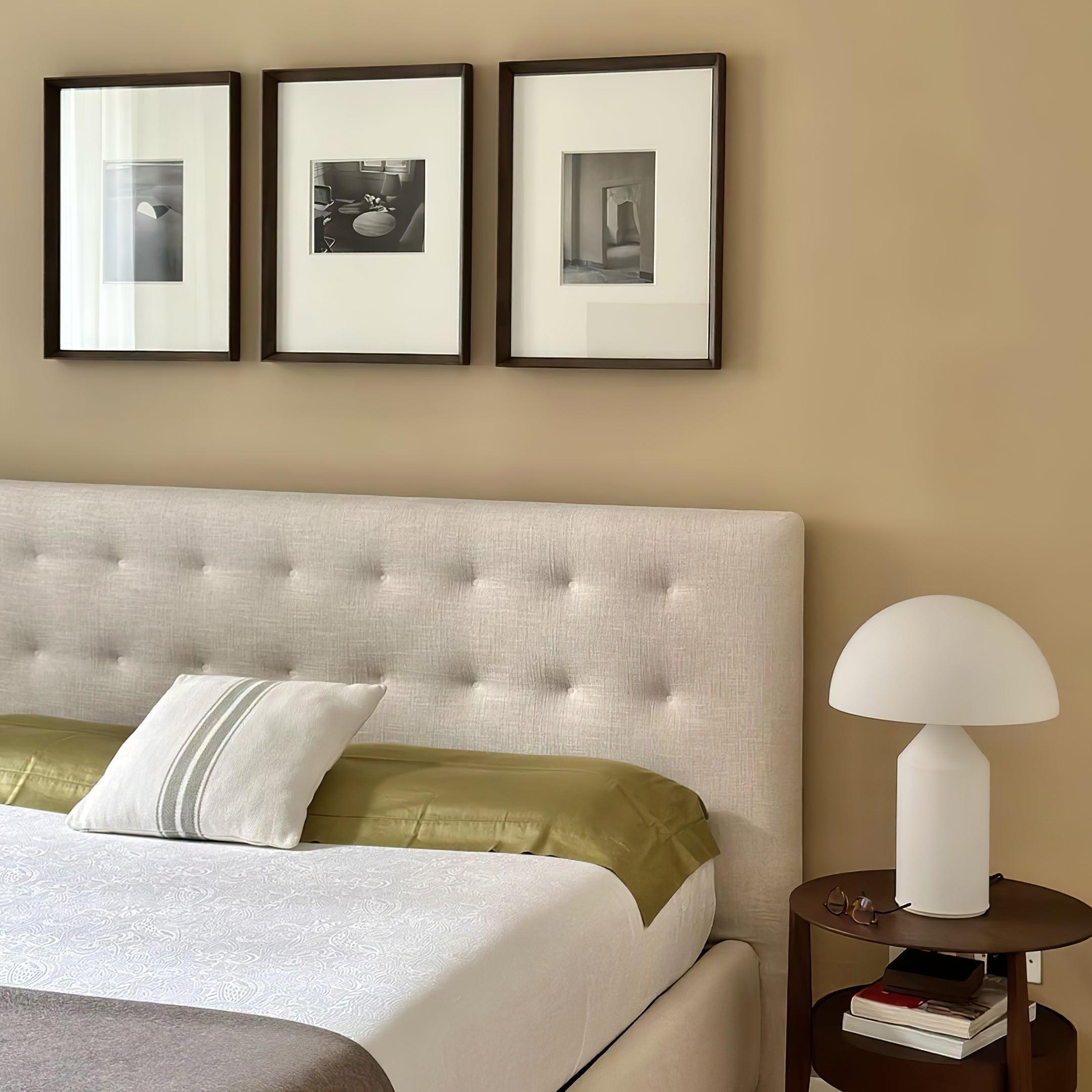 Bedroom with a tufted headboard, framed pictures on the wall, and a side table with a lamp.