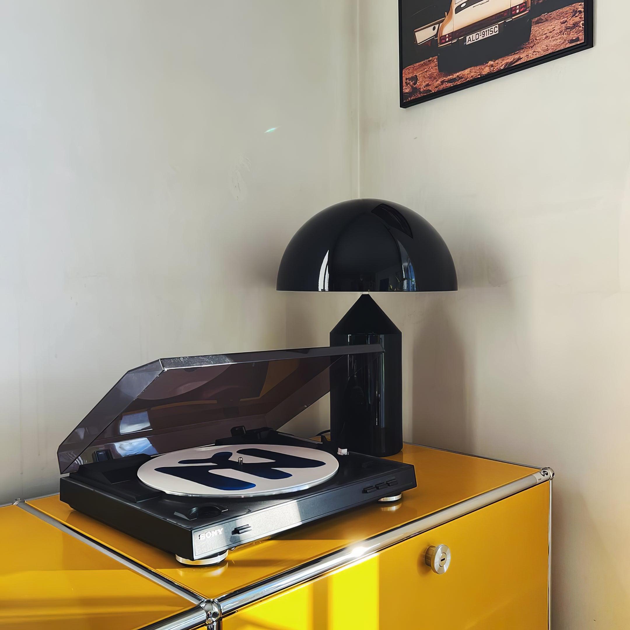 Record player on a yellow cabinet with a black lamp in the corner.