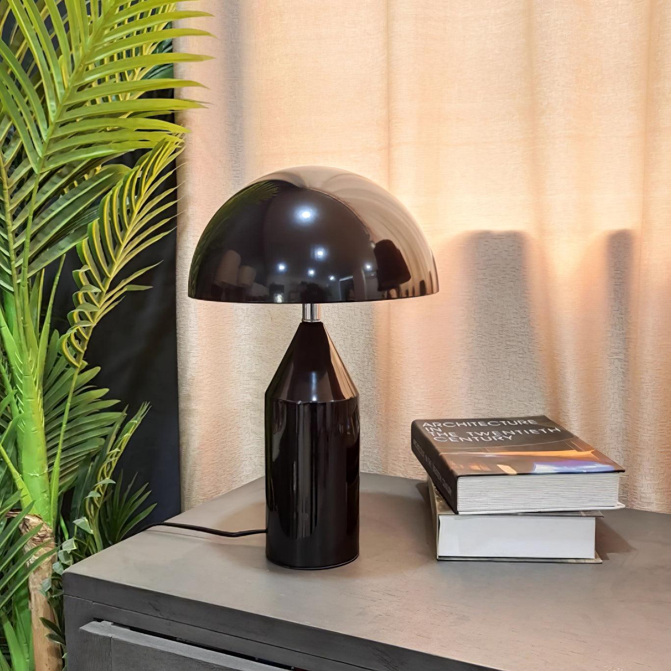 Black table lamp on a surface with books and a plant in the background