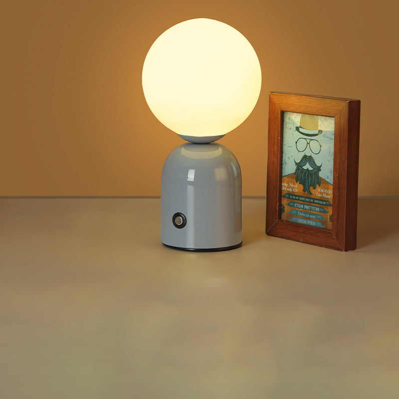 Small lamp with a round bulb on a gray base next to a framed picture on a beige surface.