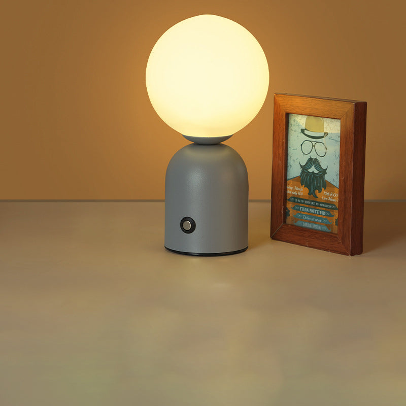 Table lamp with a round bulb on a gray base next to a framed picture on a beige surface.