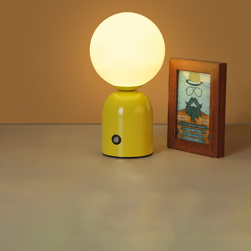 Yellow table lamp with a round white bulb next to a framed picture on a beige surface.