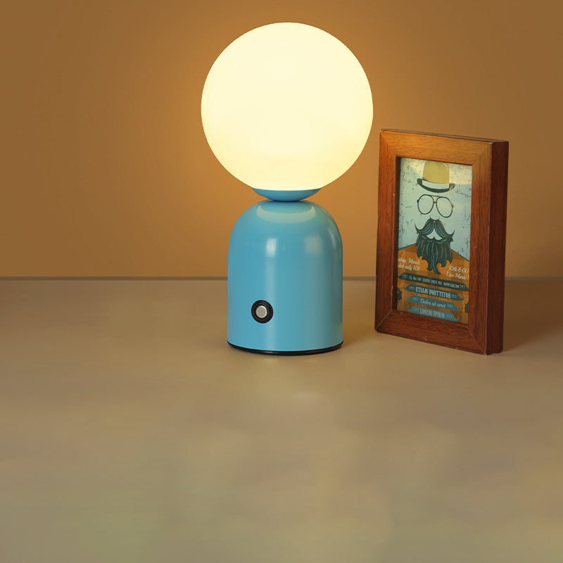 Blue table lamp with a round white bulb next to a wooden-framed picture on a beige surface.
