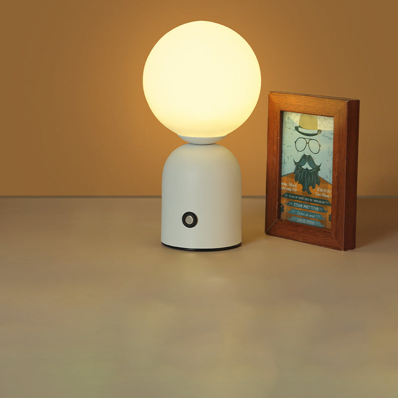 White table lamp with a round bulb next to a framed picture on a beige surface.