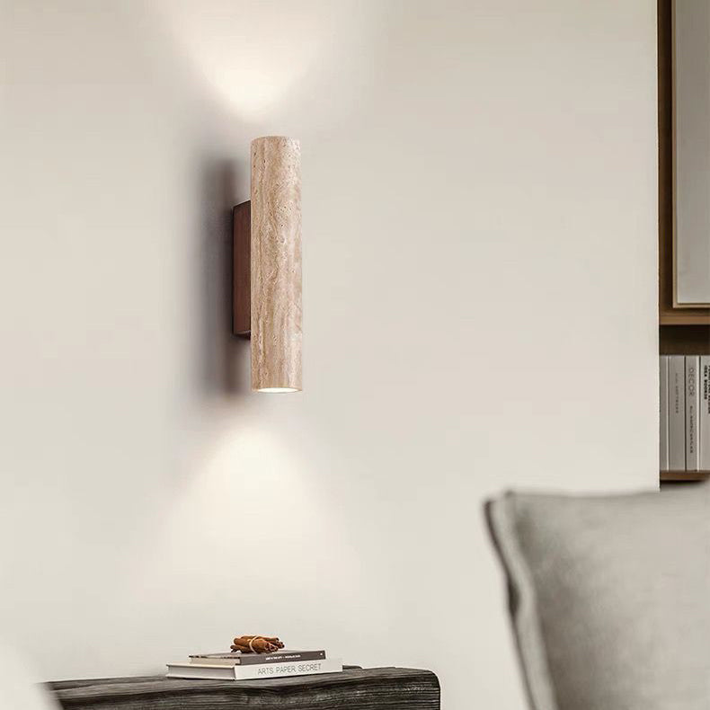 Wall-mounted cylindrical light fixture on a neutral wall with a shelf and books in the background.