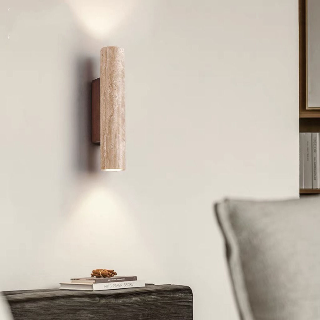 Wall-mounted cylindrical light fixture on a neutral wall with a piece of furniture below.