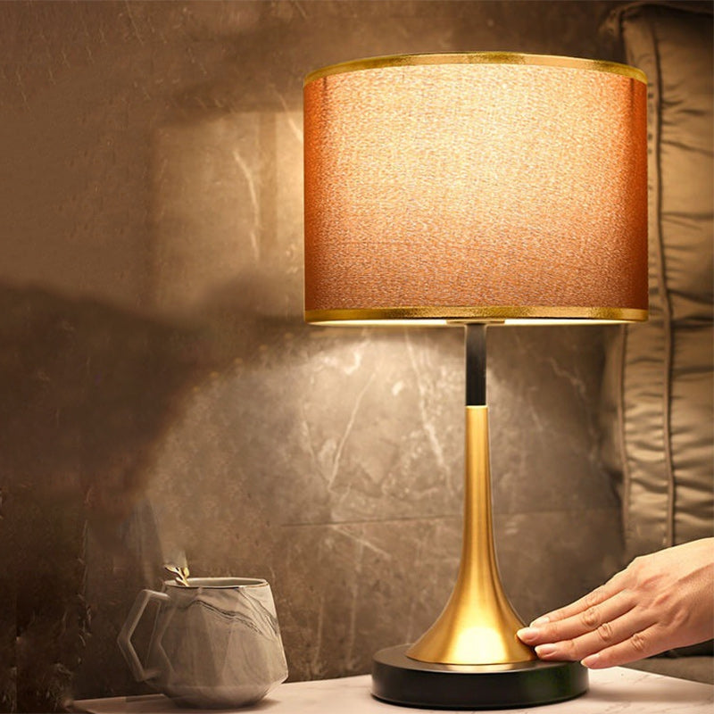 Table lamp with gold base and beige shade on a table, with a hand adjusting it.
