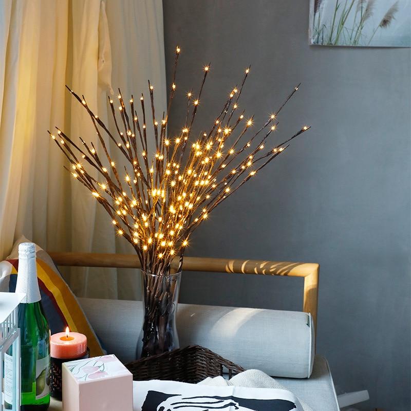 Decorative branches with lights in a vase on a table next to a bottle and candle.