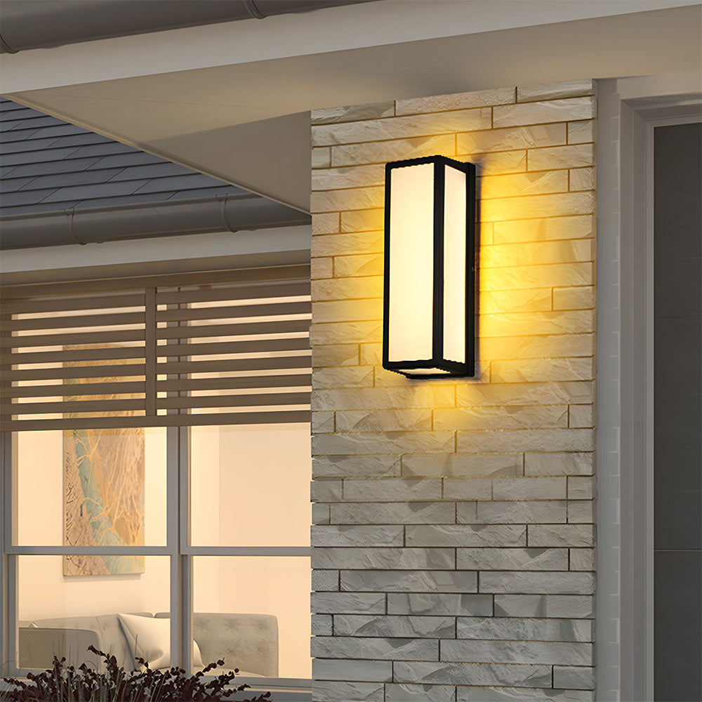Wall-mounted outdoor light fixture on a stone wall with a window and interior decor in the background.