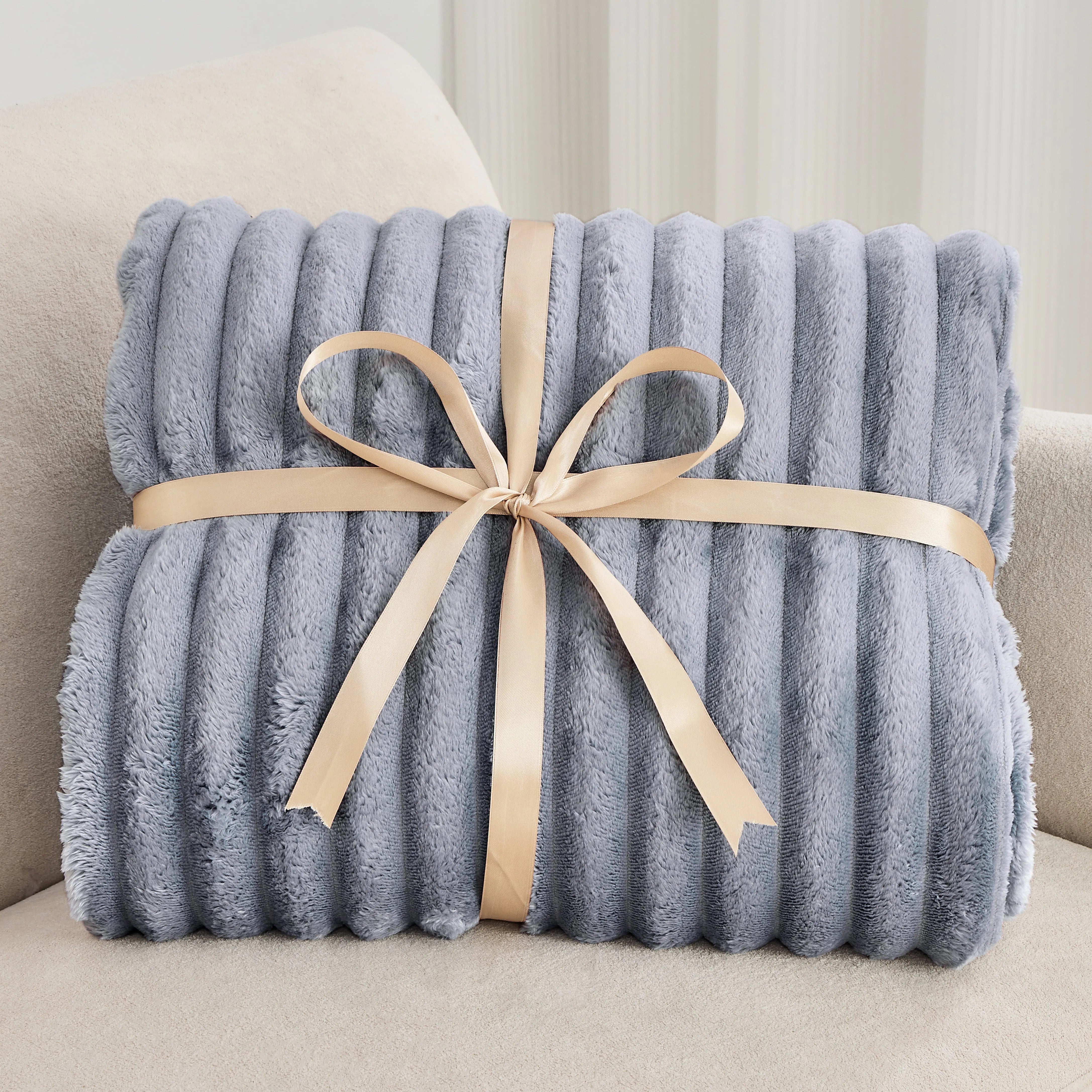 Gray plush blanket with a beige ribbon on a light-colored couch