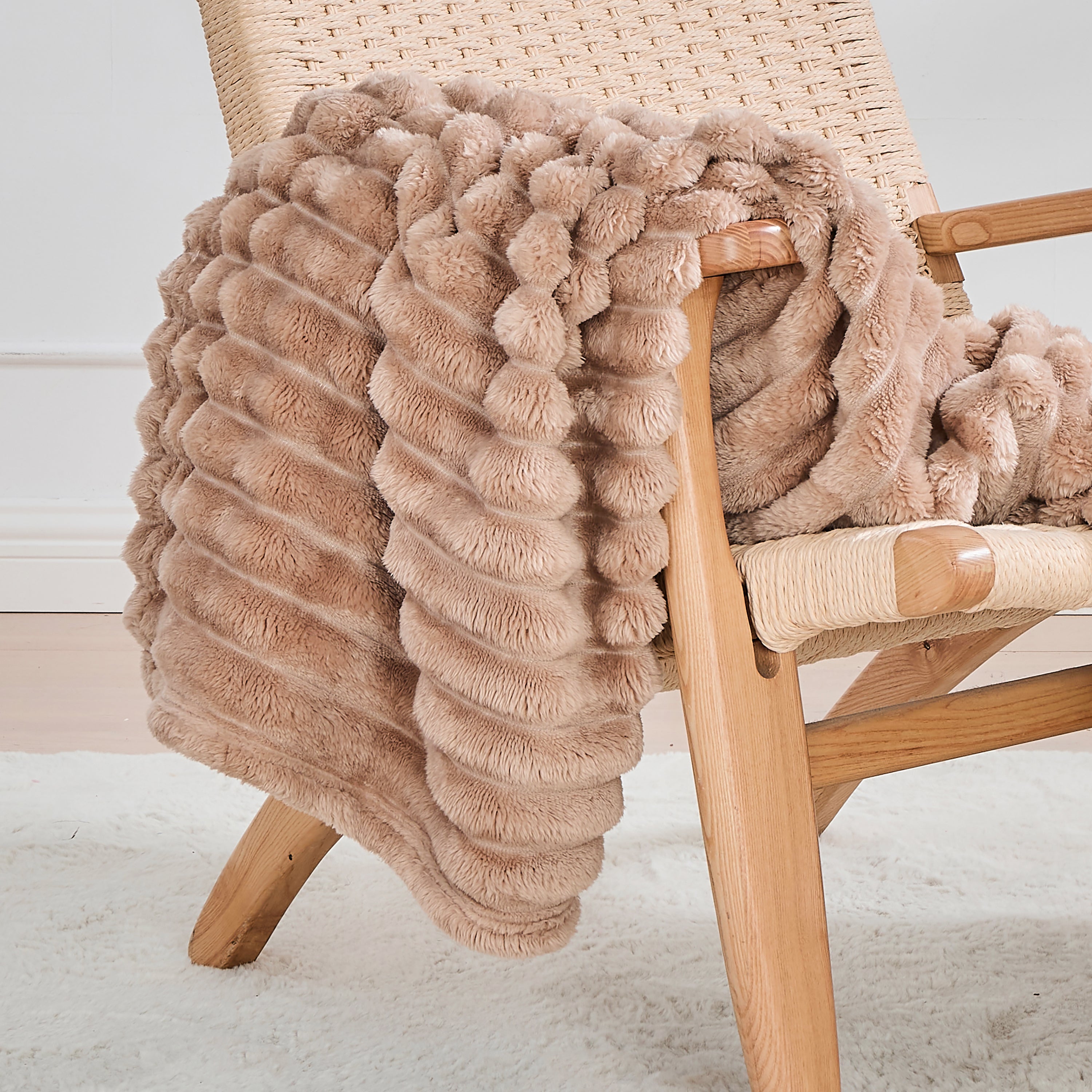 Beige faux fur throw blanket draped over a wooden chair on a light background