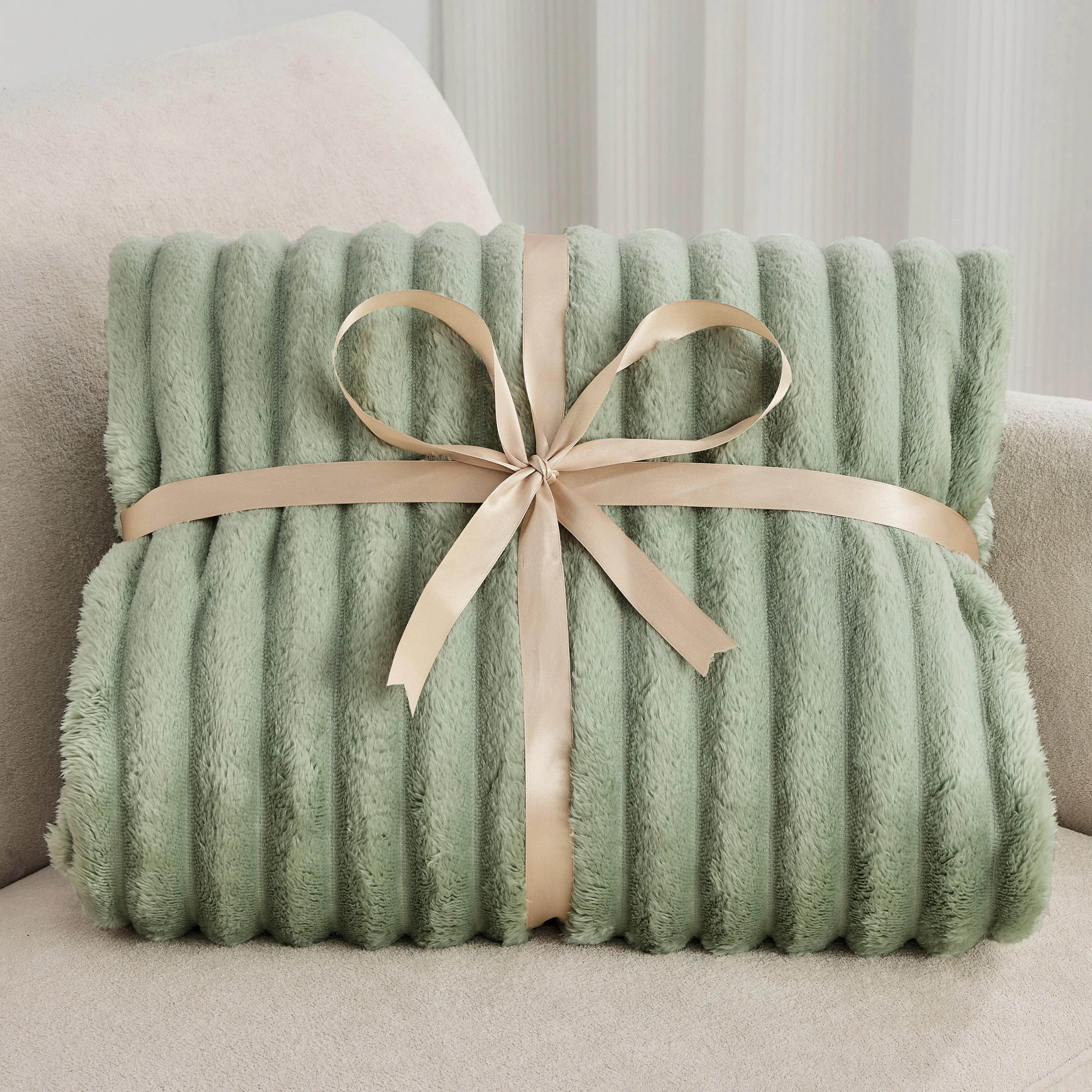 Green plush blanket with a beige ribbon on a light-colored couch.