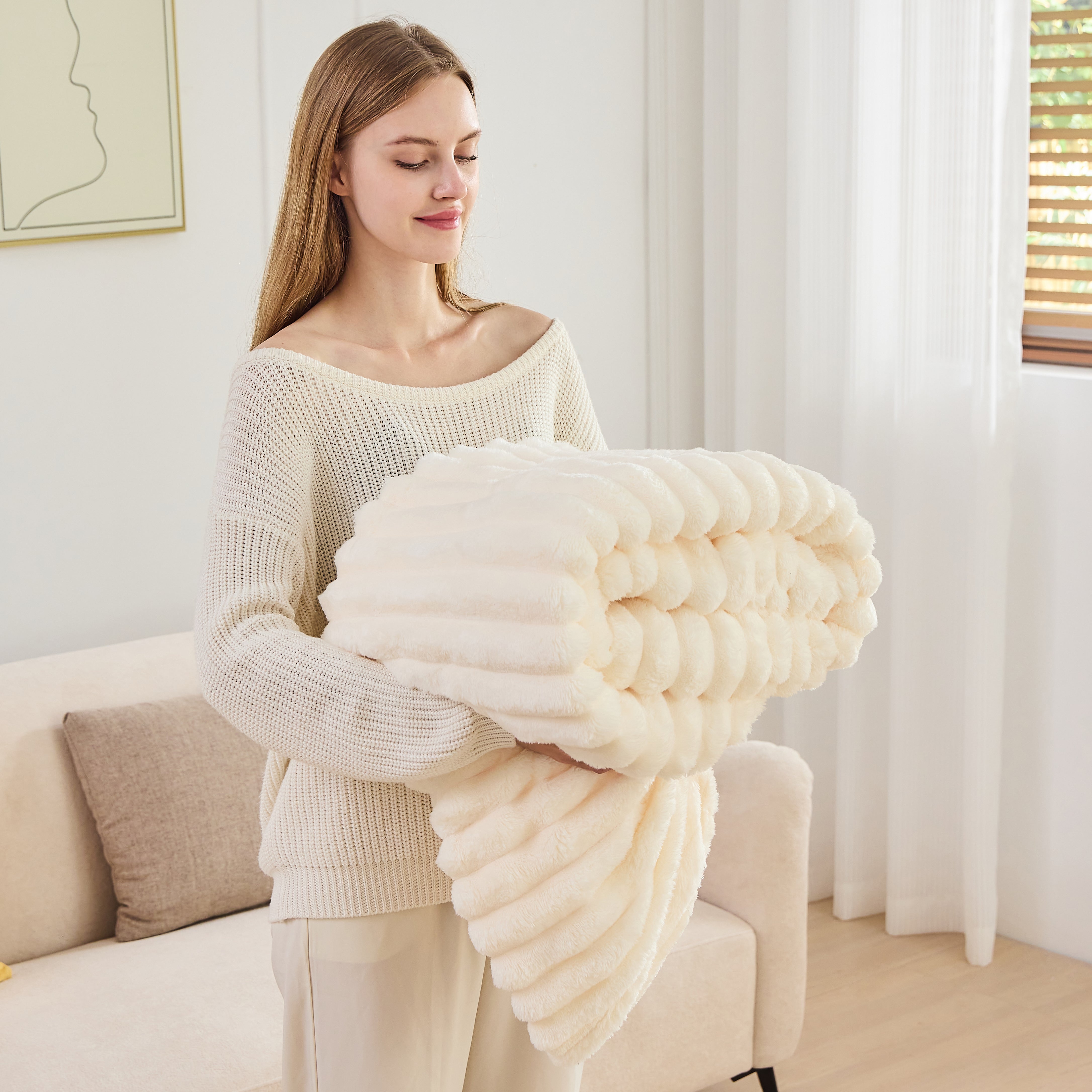 Woman holding a large, fluffy white blanket in a bright living room.
