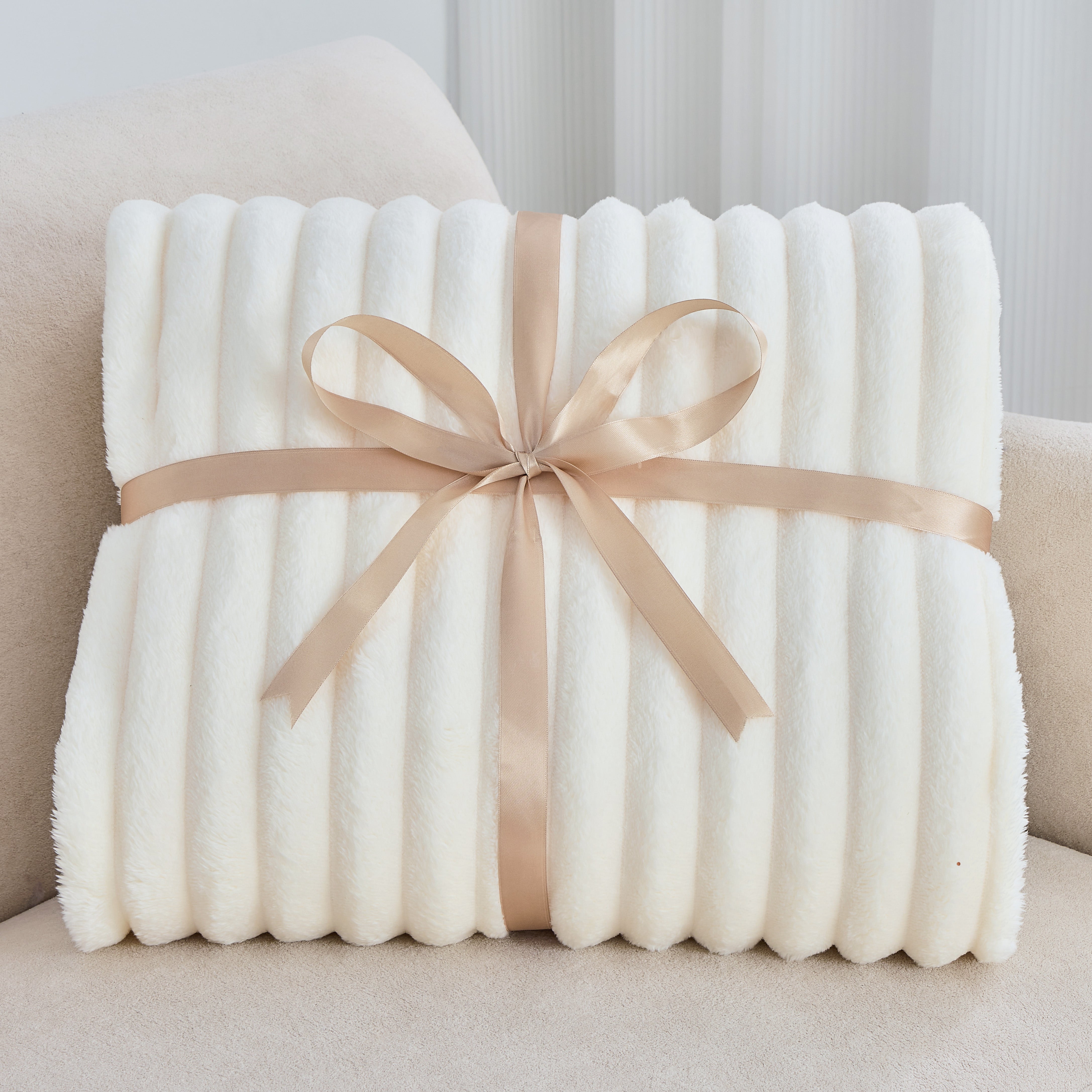 White plush blanket with a beige ribbon on a light-colored couch.