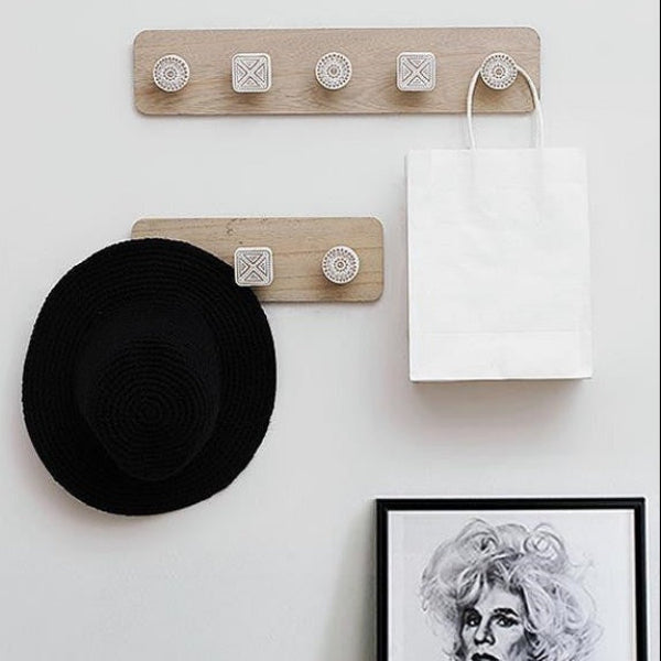 Wooden wall hook with a black hat and white bag on a white wall.