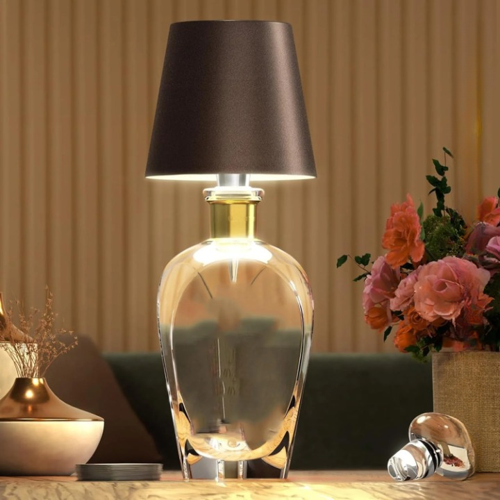 Decorative table lamp with a black shade on a wooden surface, surrounded by flowers and other decorative items.