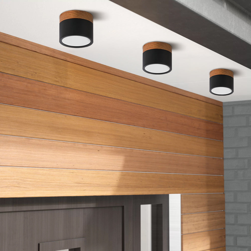 Modern cylindrical ceiling lights with a black and wood finish above a wooden wall.