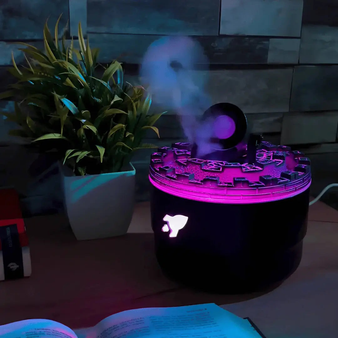 Black diffuser emitting purple mist on a table with a plant and book in the background