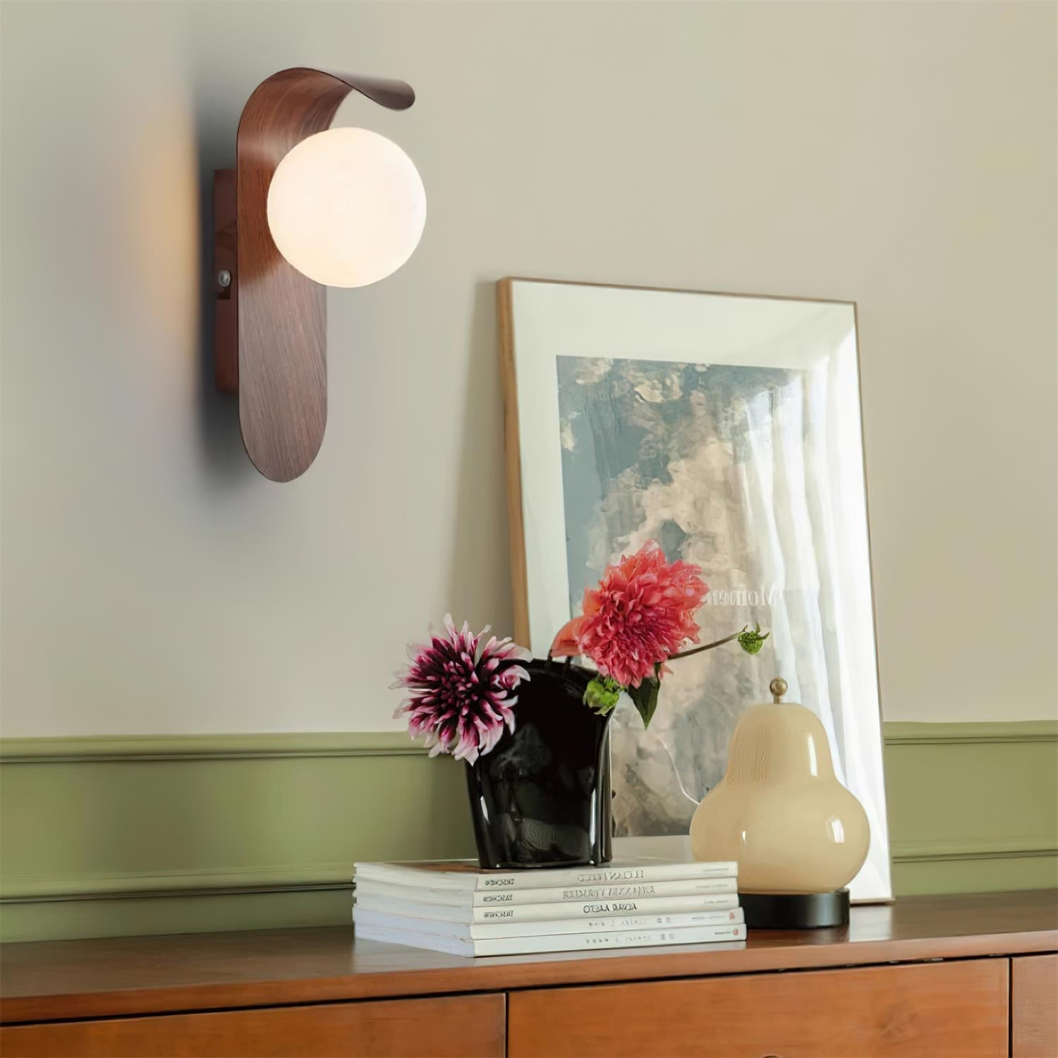 Wall-mounted lamp, books, and decorative items on a wooden surface with a neutral background