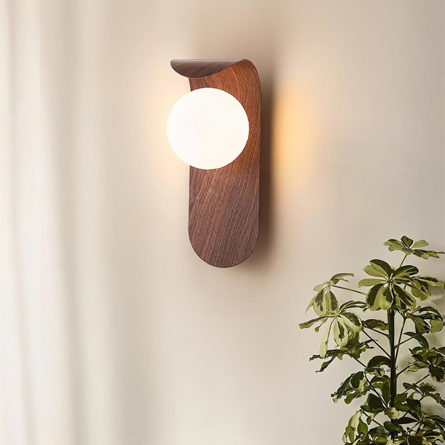 Wooden wall sconce with a round light bulb on a neutral wall, next to a plant and books on a wooden surface.
