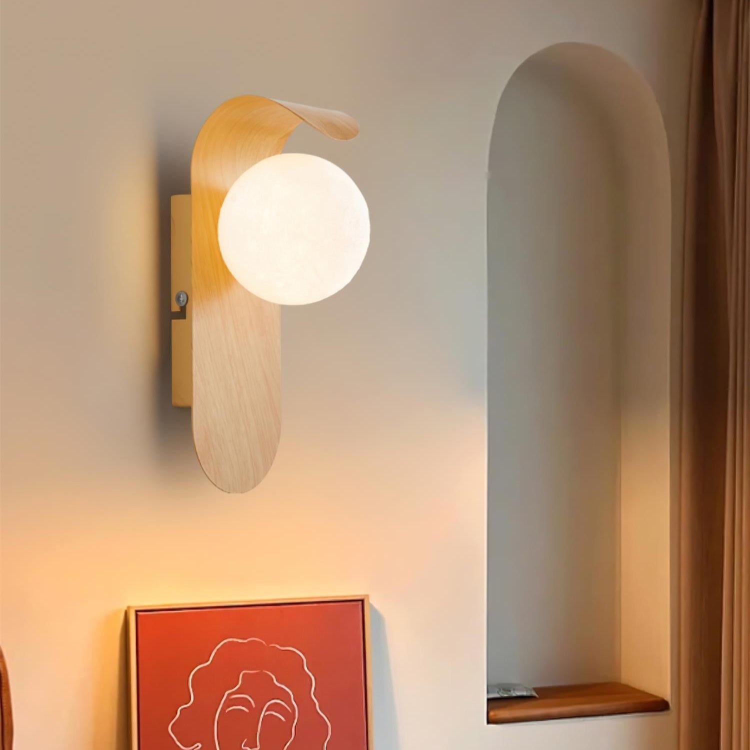Modern wall lamp with a round bulb on a neutral wall, next to a framed artwork of a woman's face.
