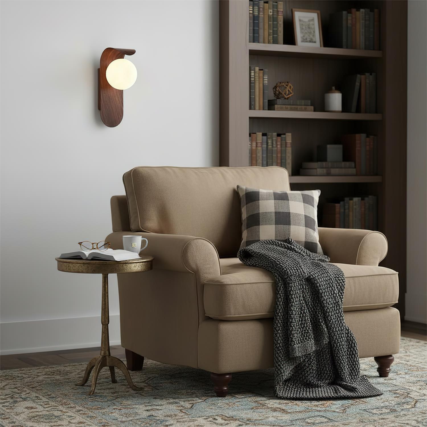Beige armchair with plaid pillow and blanket in a cozy room with bookshelf and side table.