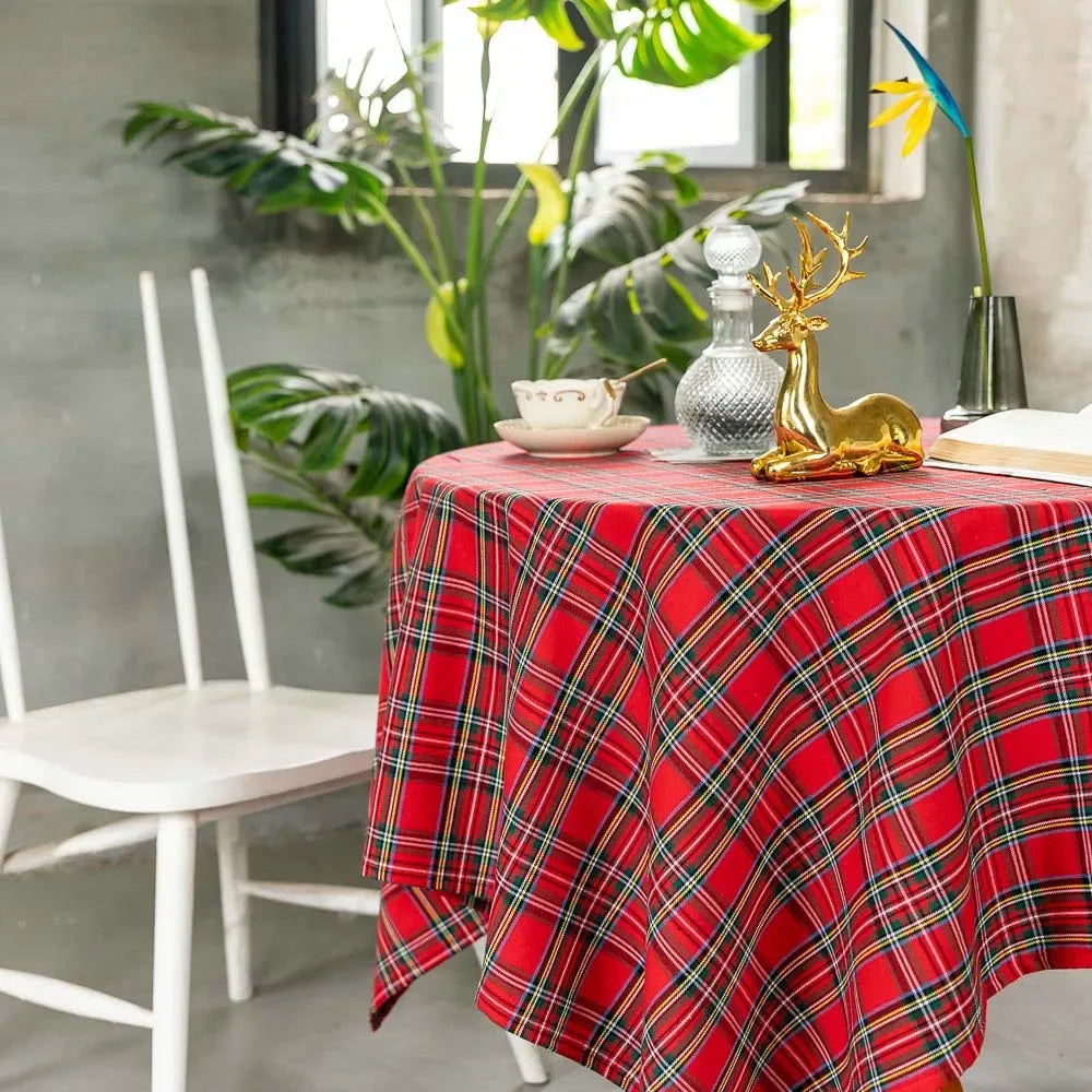 Round table with a red plaid tablecloth, gold deer ornament, and white chair in a room with plants.