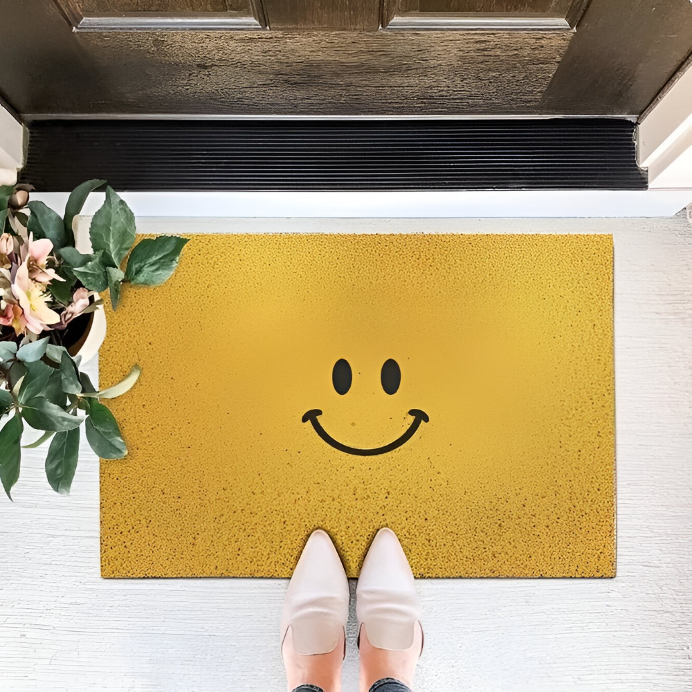 Yellow doormat with a smiley face design in front of a wooden door.