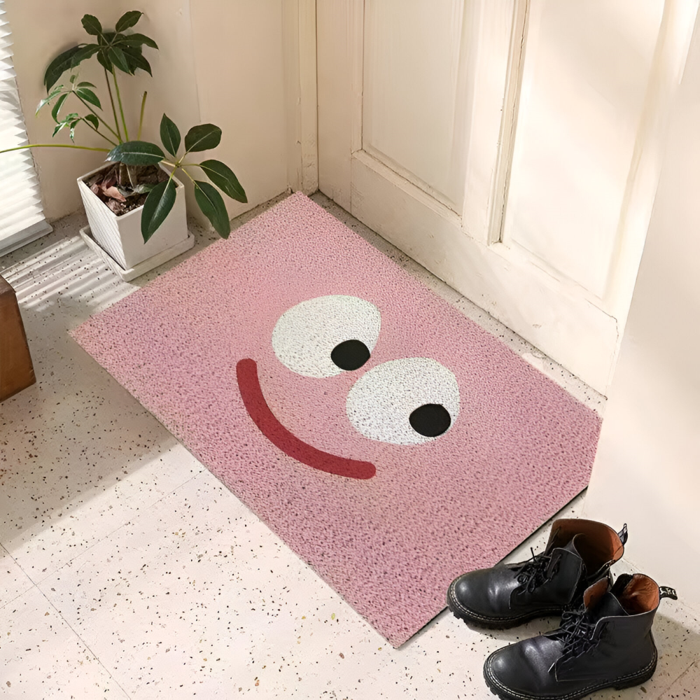 Pink doormat with smiley face design on a tiled floor next to a plant and shoes.