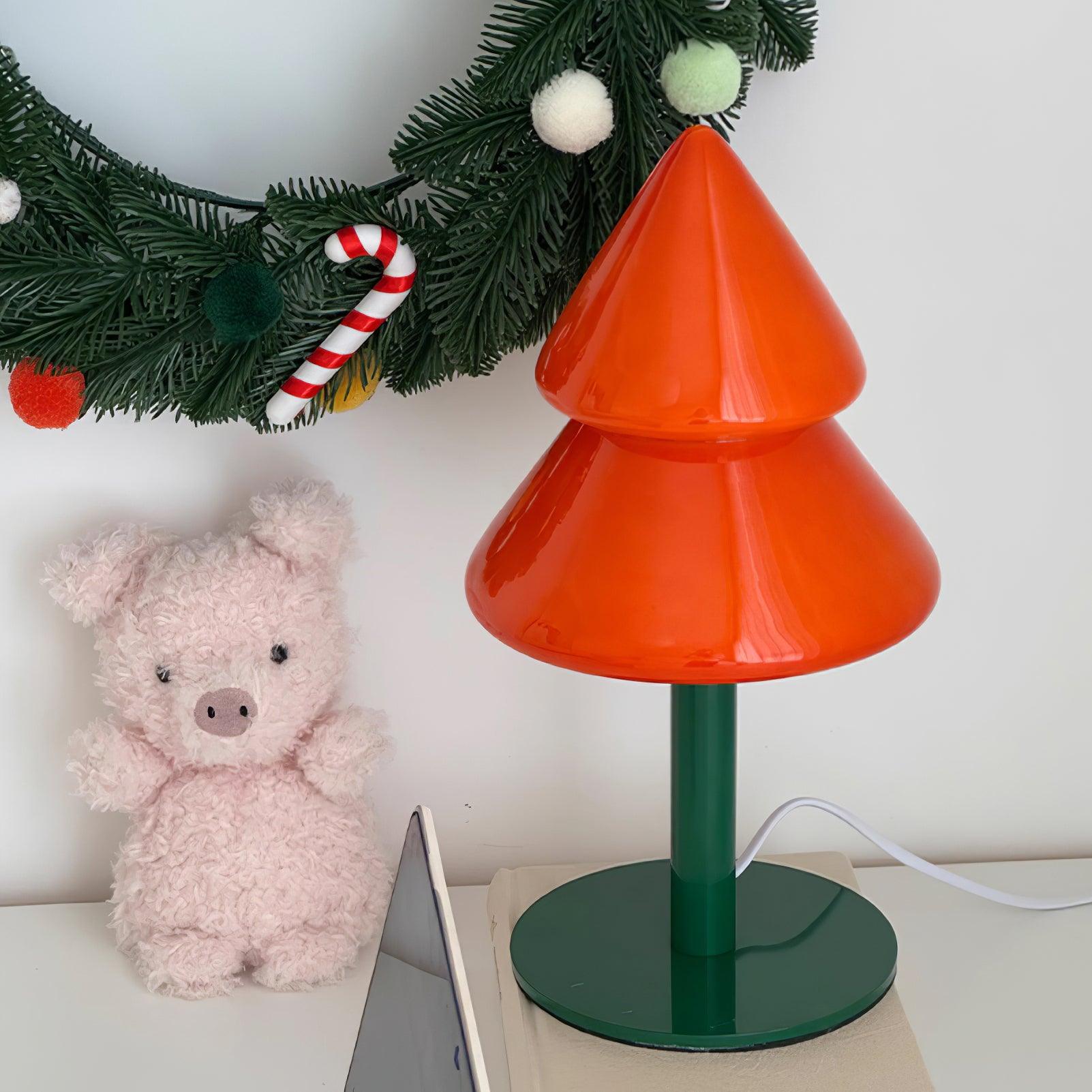 Orange Christmas tree-shaped lamp with a green base next to a pink teddy bear and festive decorations.