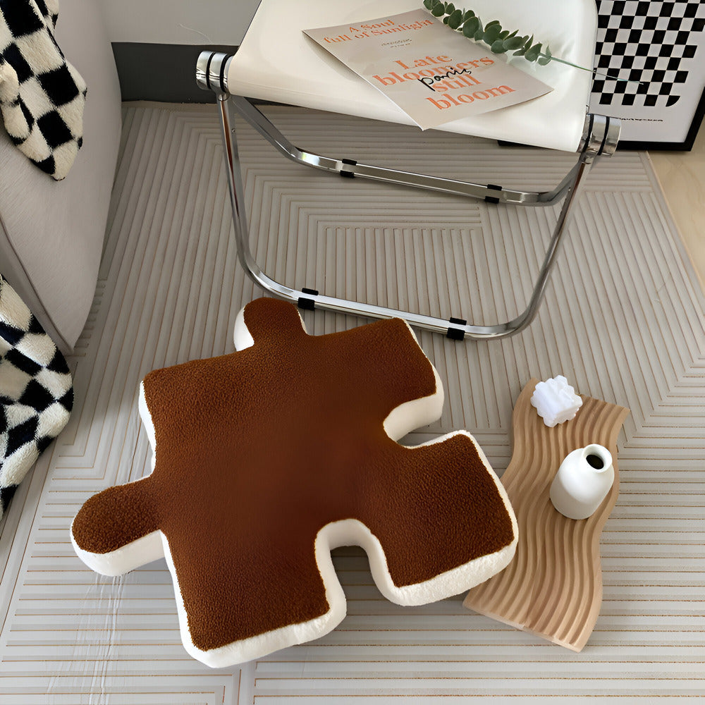 Brown puzzle piece-shaped cushion on a textured floor with a chair and magazine in the background.
