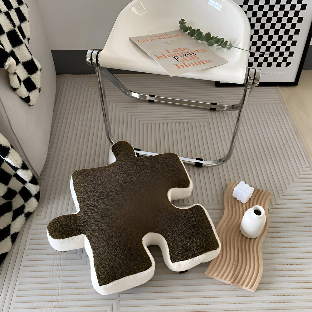 Brown puzzle piece-shaped cushion on a checkered floor with a chair and decorative items in the background.