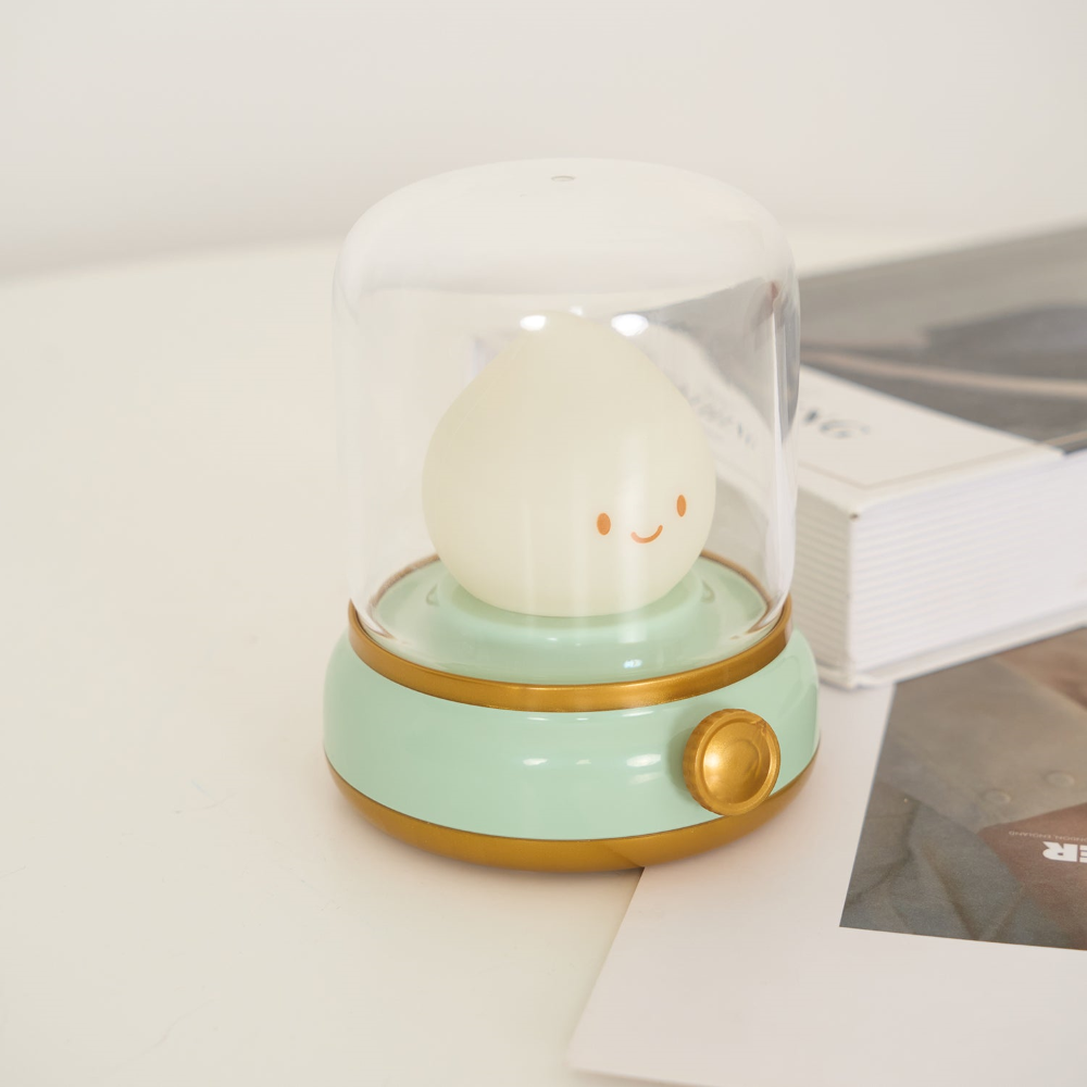 Small round lamp with a smiling face on a light green base, sitting on a surface.