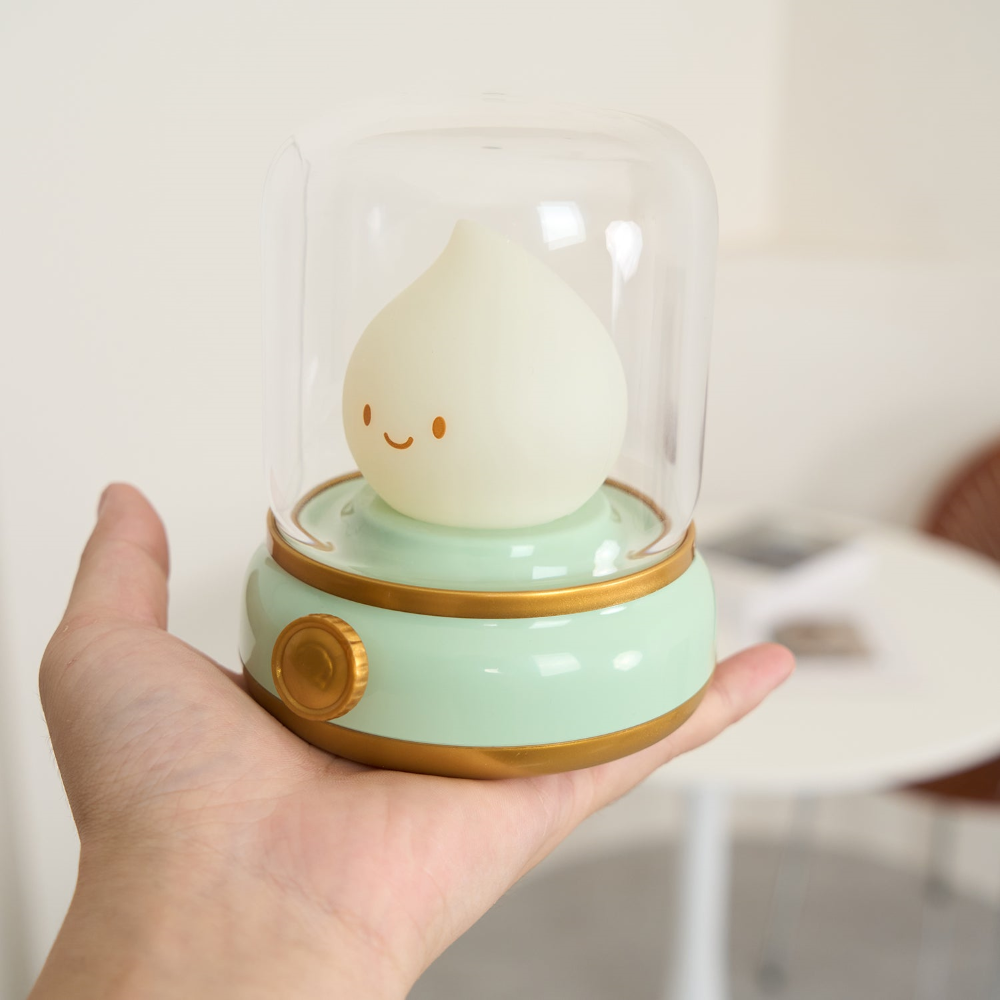 Cute light bulb figurine with a smiling face inside a glass dome held in a hand.