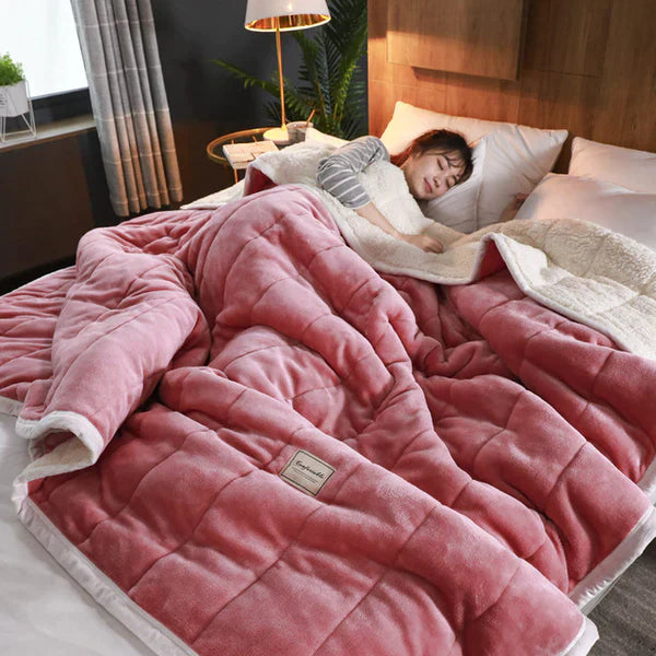 Person lying in bed under a pink weighted blanket with a blurred background