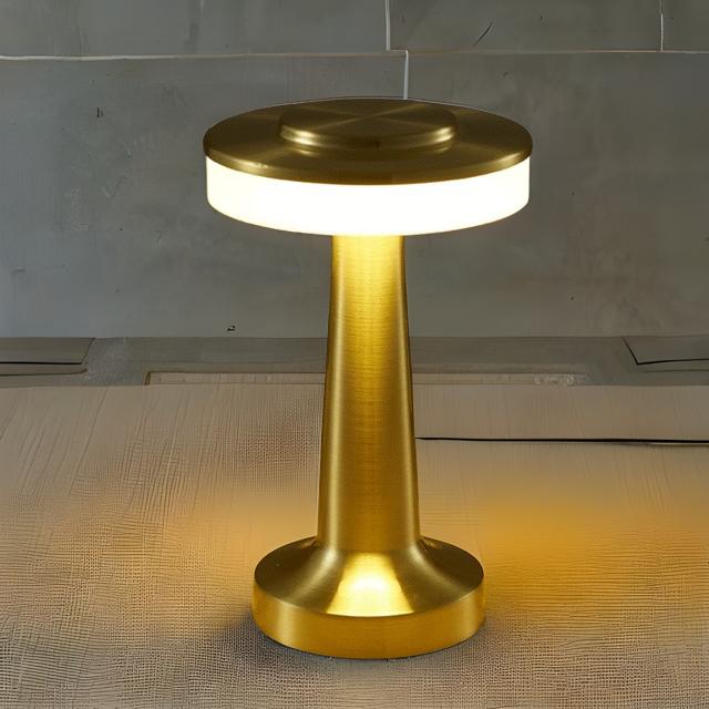 Gold-colored lamp with a round base and cylindrical body on a textured surface.