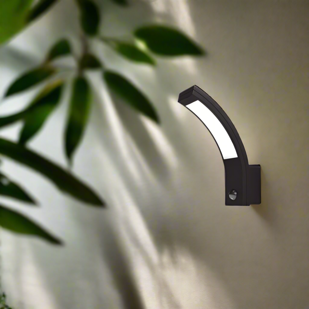 Black outdoor wall light fixture on a light-colored wall with green leaves in the foreground.