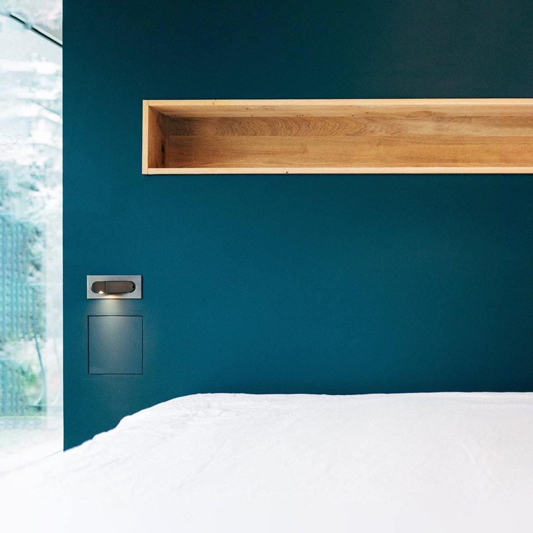 Modern bedroom with teal wall, wooden shelf, and white bedding.
