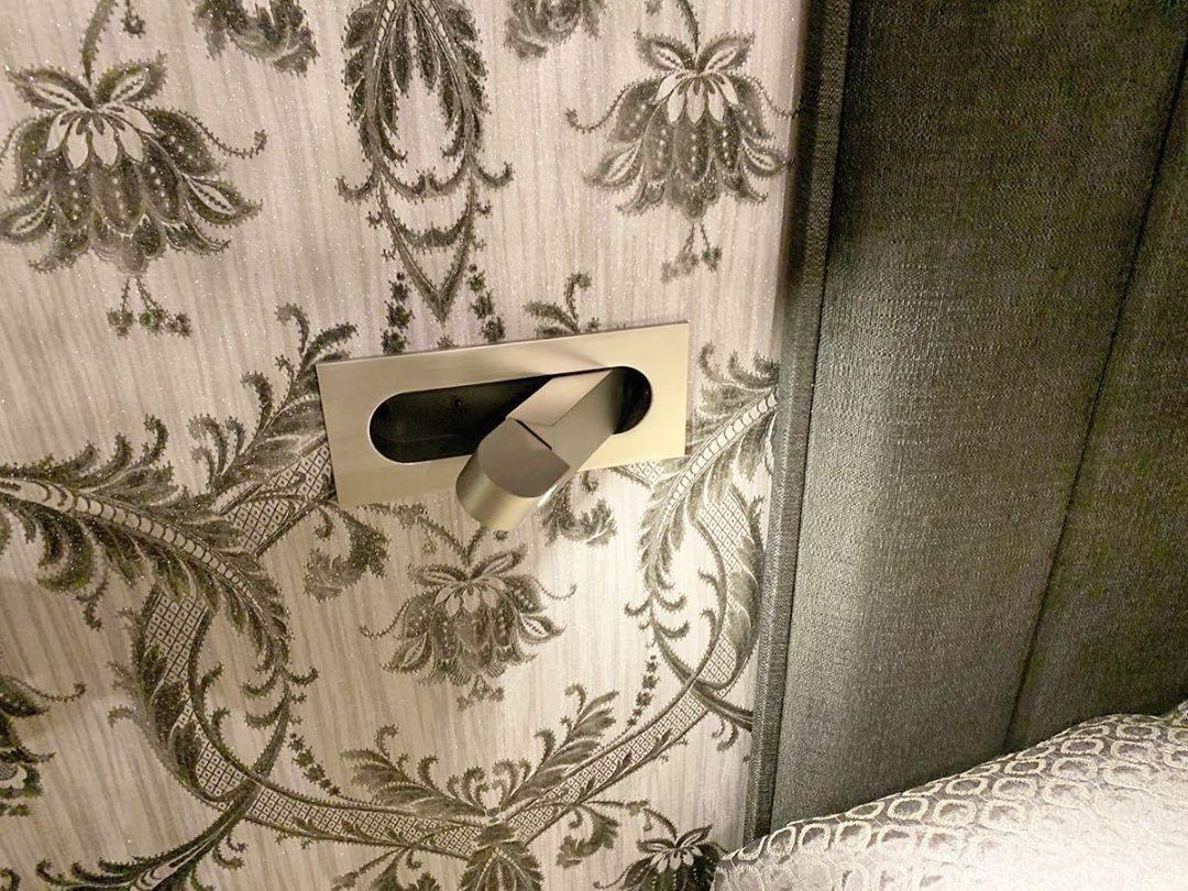 Decorative wall switch plate with floral wallpaper and gray upholstered chair.
