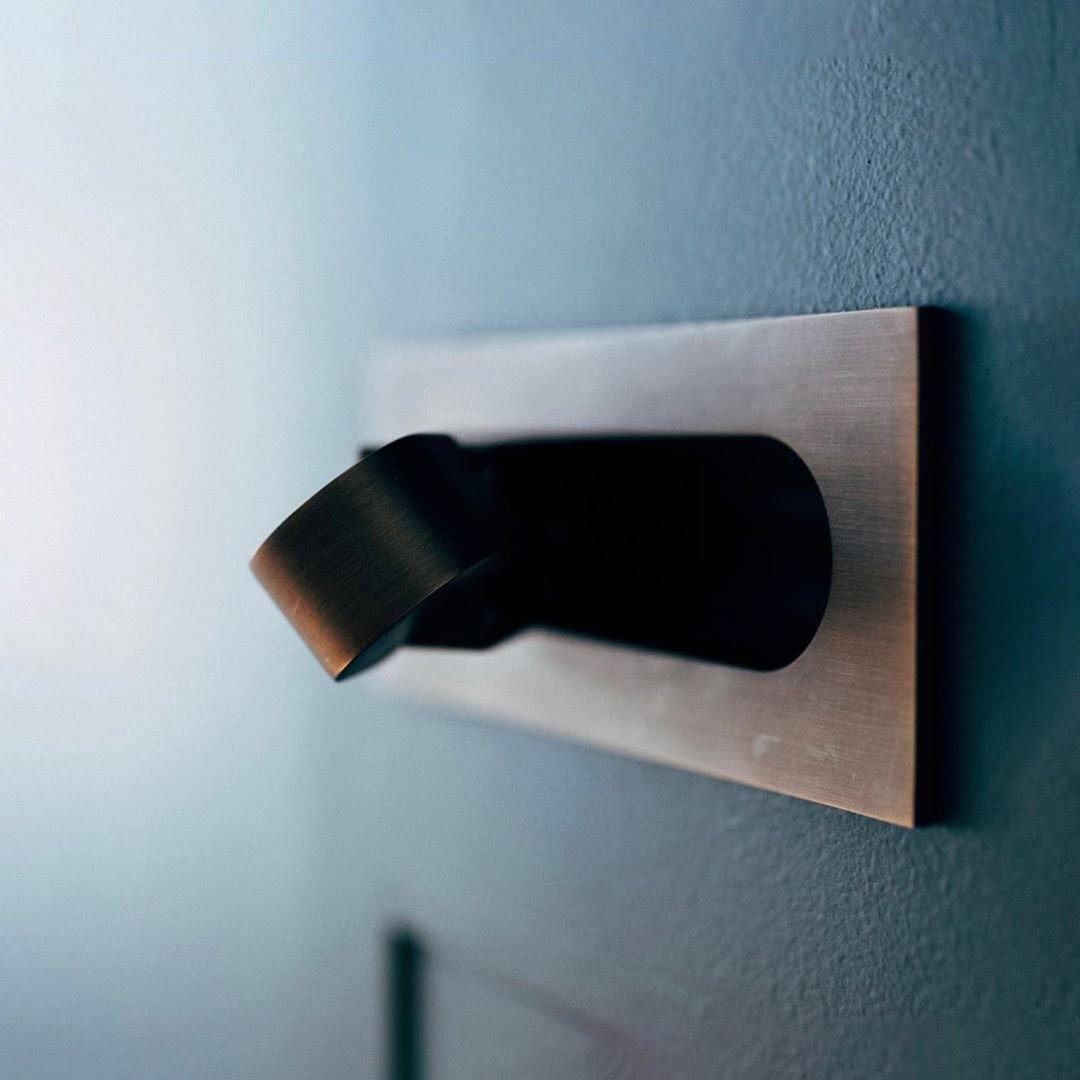 Metallic wall-mounted fixture with a black component on a blue wall.