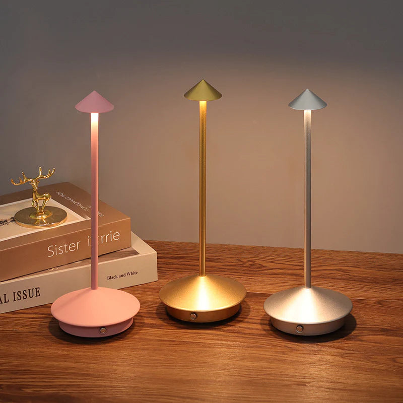 Three colorful desk lamps on a wooden surface with books in the background.