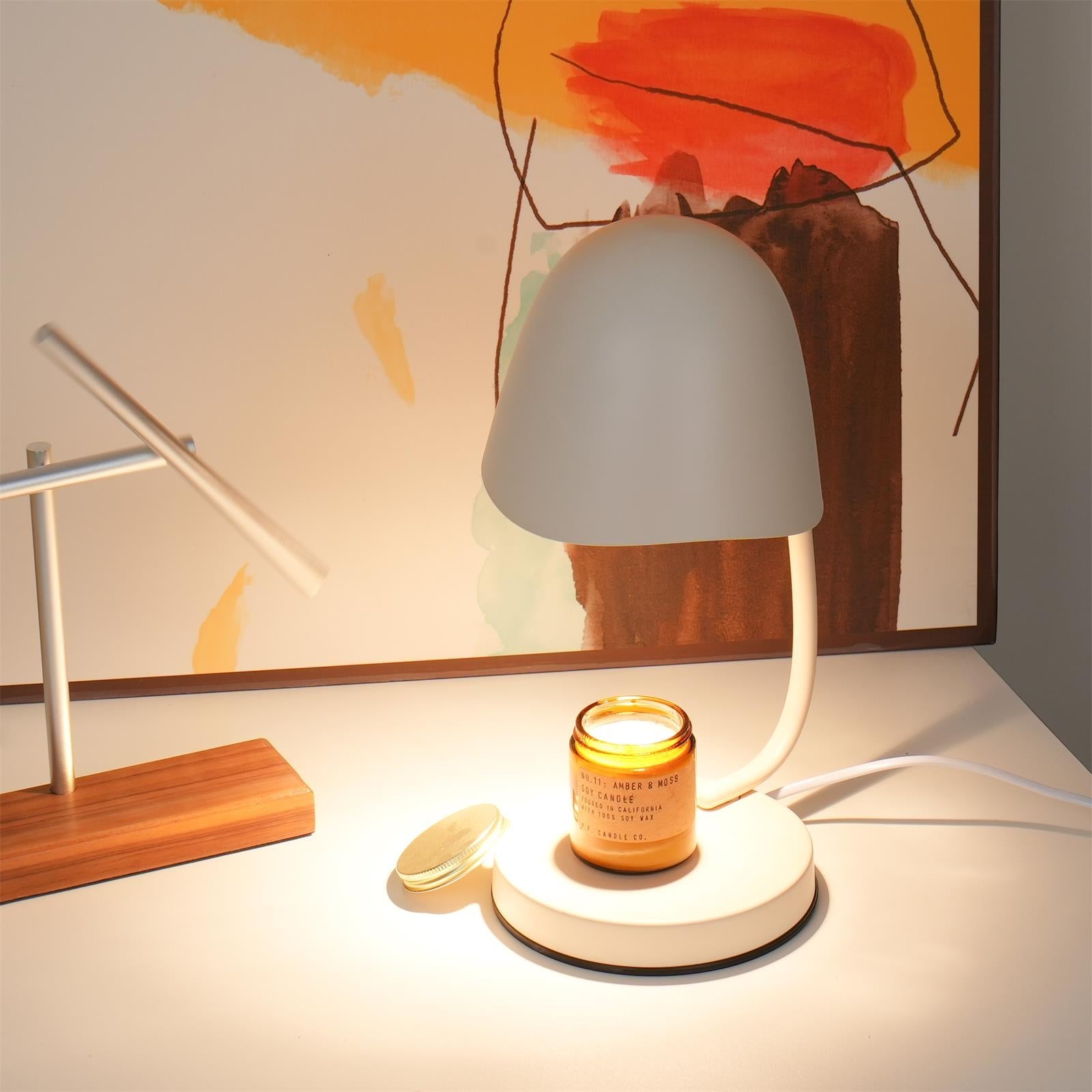 Table lamp with a candle on a white surface, with abstract art in the background