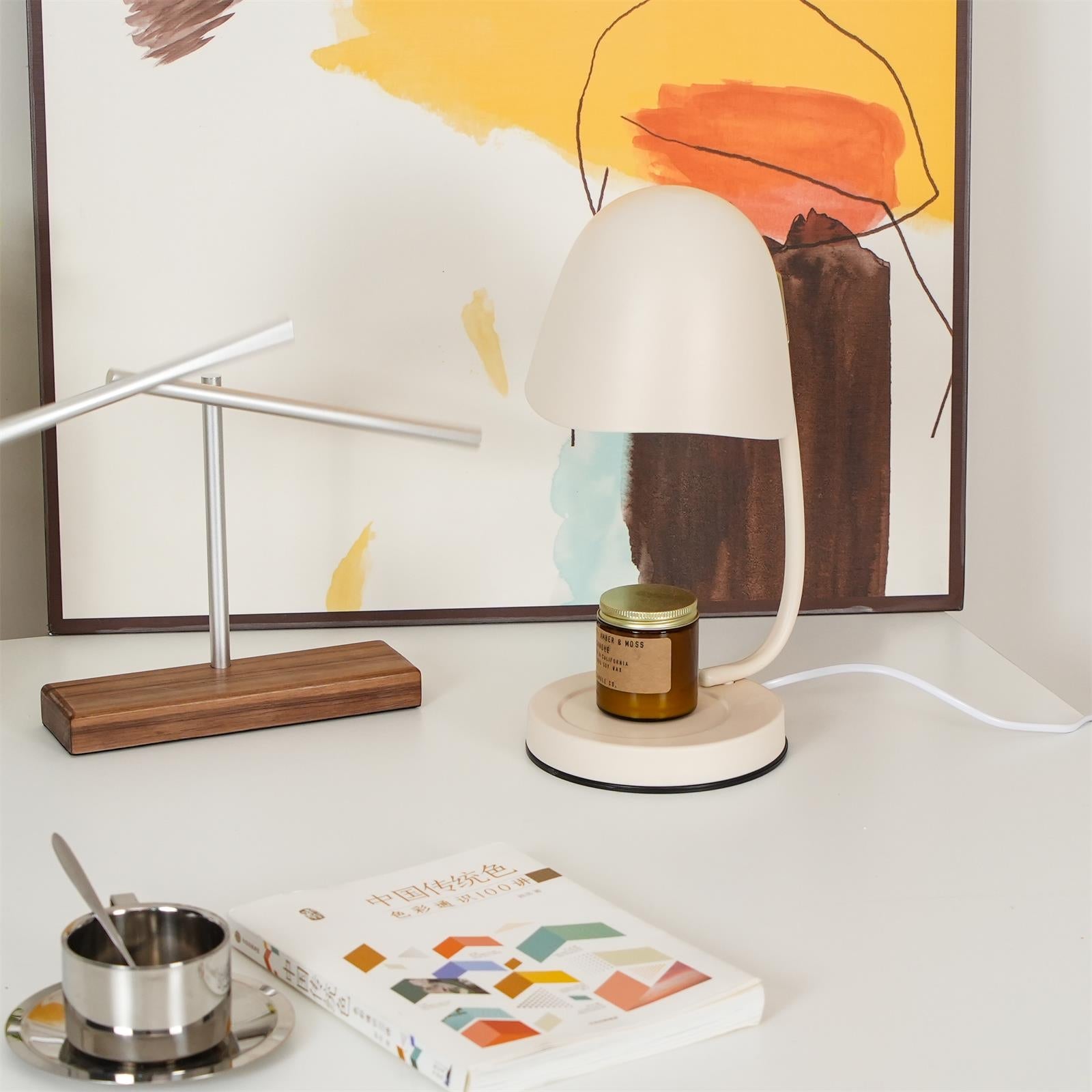 Desk setup with a lamp, notebook, and small container against a colorful abstract painting.