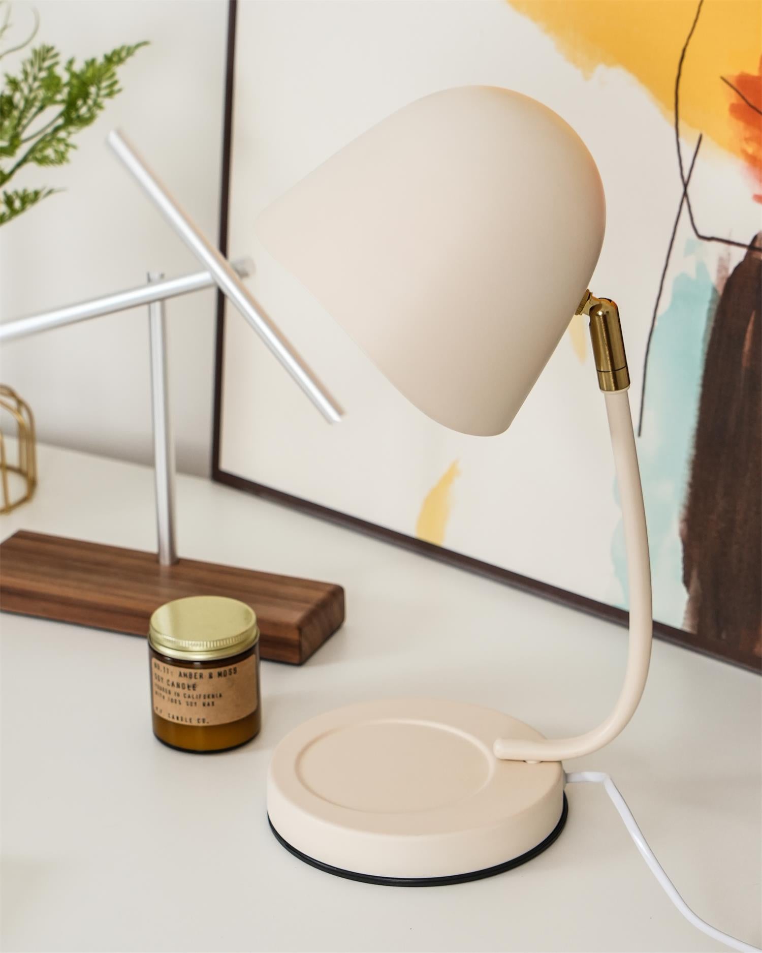 Beige desk lamp on a white surface with a framed picture and candle in the background