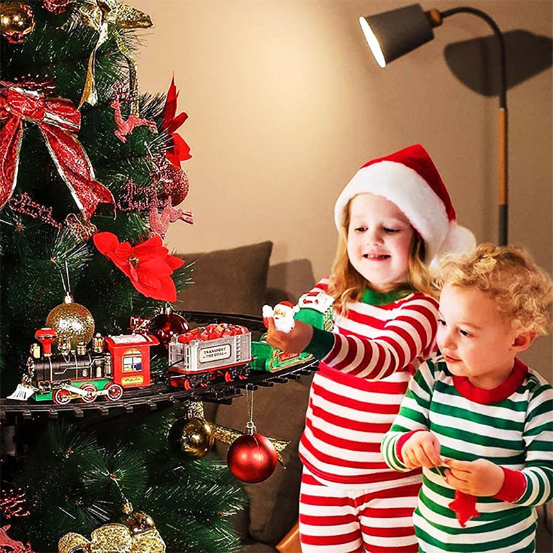 Two children in matching striped pajamas standing next to a decorated Christmas tree with a small train set.