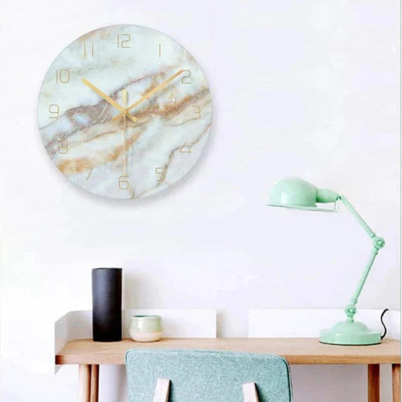 Marble-patterned wall clock on a white wall above a wooden desk with a lamp and chair.