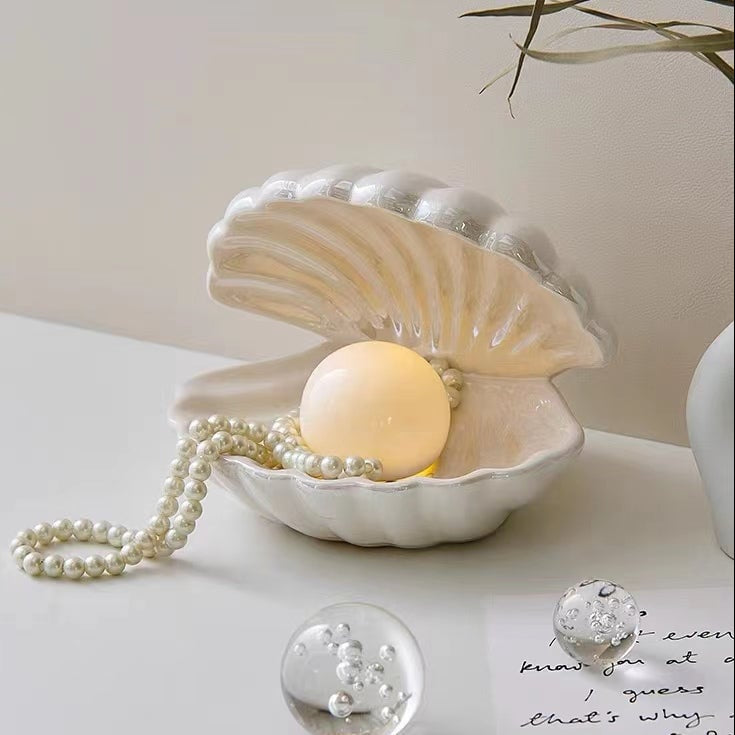 Pearl necklace and bath bomb inside a seashell on a light surface.