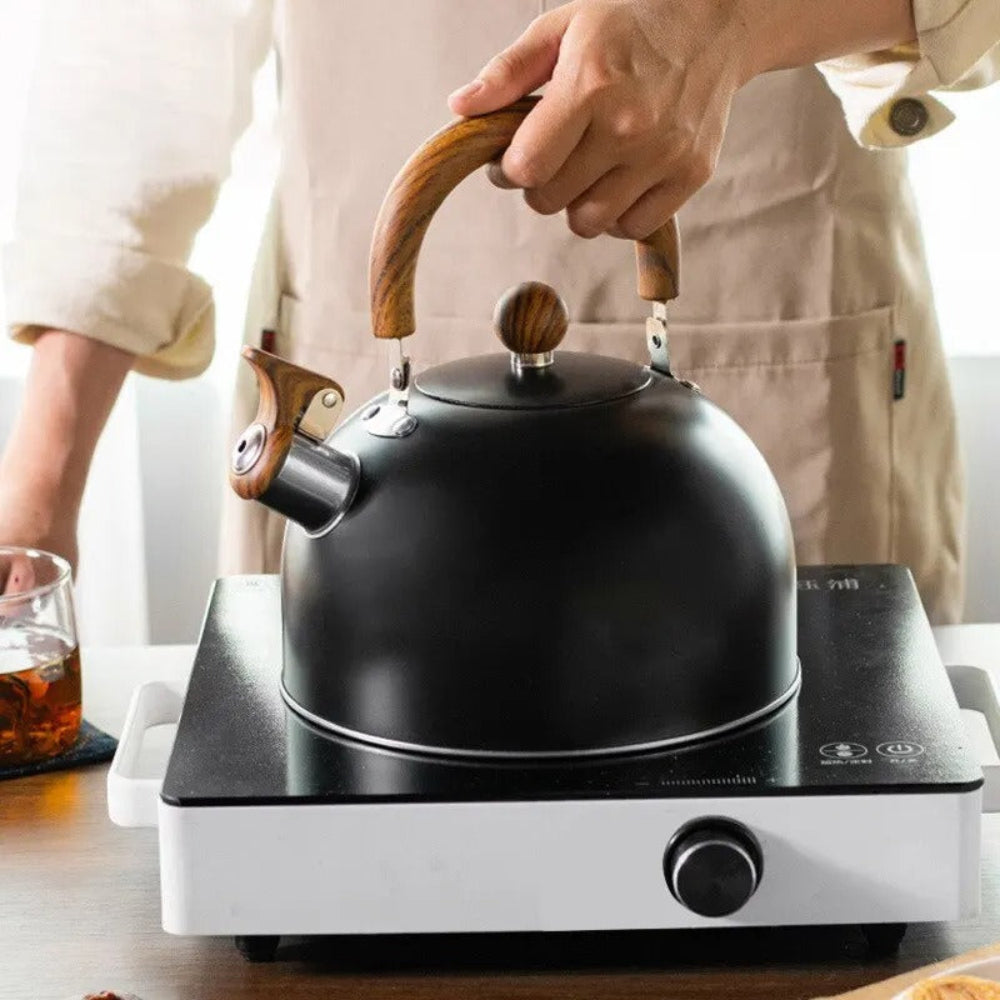 Person holding a black kettle with wooden handle on a hot plate