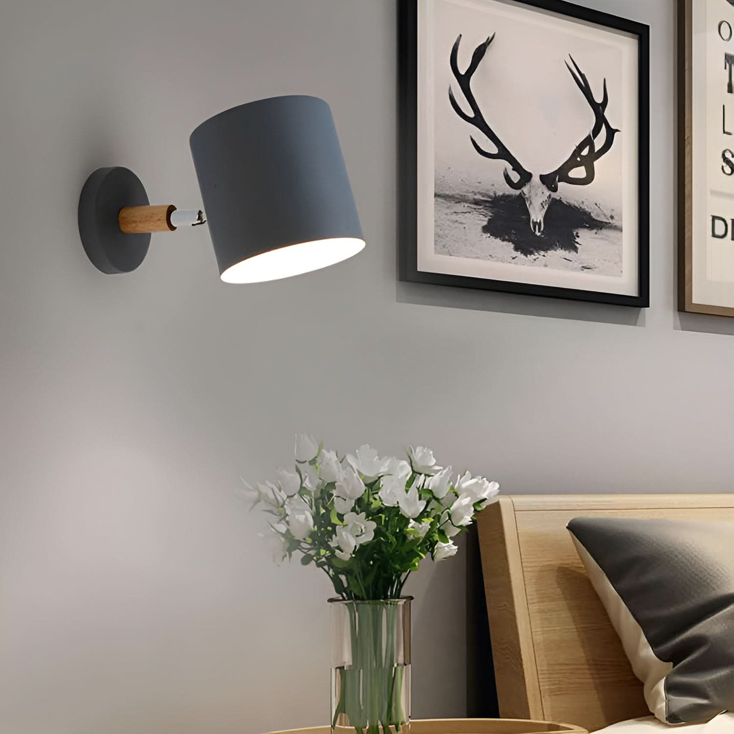 Wall-mounted lamp with a vase of flowers on a bedside table, with a deer head artwork in the background.