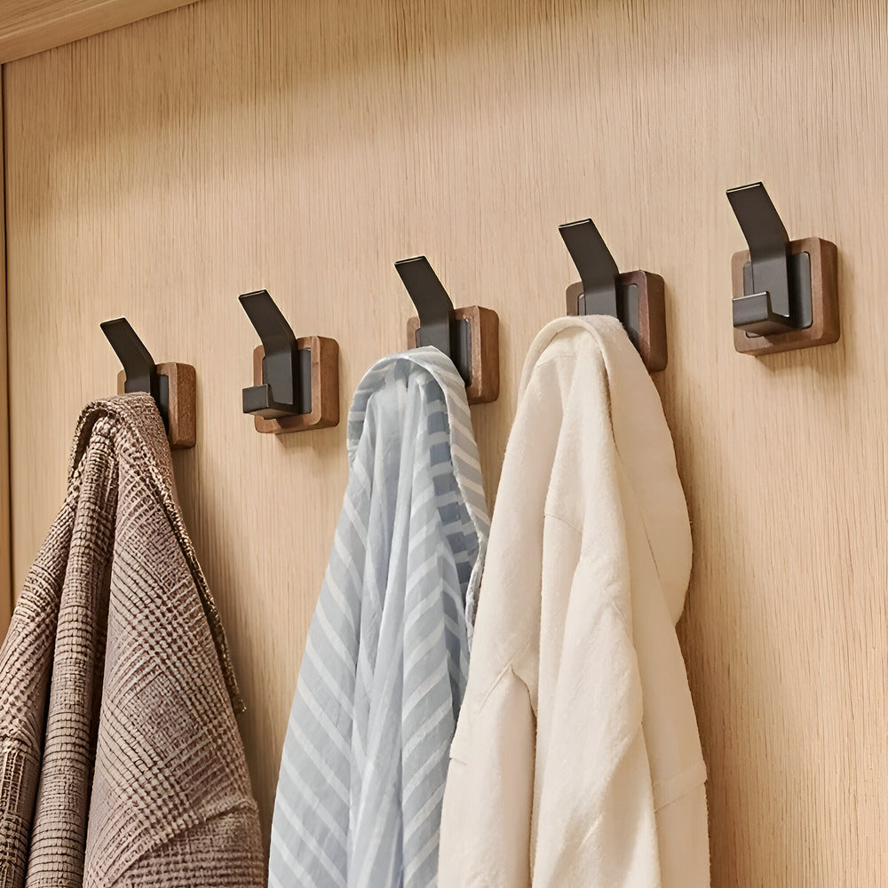 Four wooden hooks on a wall with coats hanging from them.